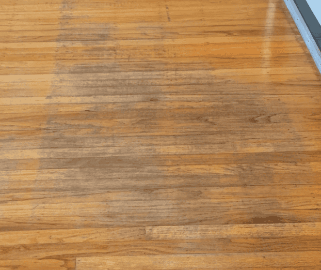 A wooden gym floor with a wide strip of visible dirt or wear running down the middle, contrasting with cleaner wood on the sides.